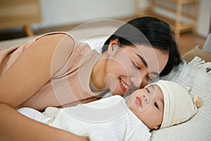 Beautiful asian mom lay down with her baby, comforting her son on bed