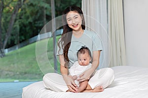 Beautiful Asian mom woman holding newborn baby in her arms sit on bed at white cozy home.Happy infant baby smile in mother arms