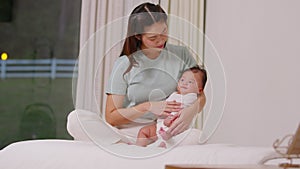 Beautiful Asian mom woman holding newborn baby in her arms sit on bed at white cozy home.Happy infant baby smile in mother arms