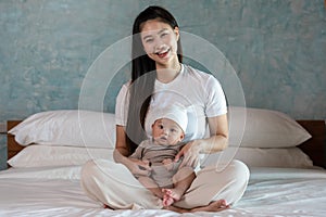 Beautiful Asian mom woman holding newborn baby in her arms sit on bed at white cozy home.Happy infant baby smile in mother arms