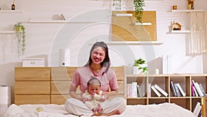 Beautiful Asian mom woman holding newborn baby in her arms sit on bed at white cozy home.Happy infant baby smile in mother arms