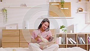 Beautiful Asian mom woman holding newborn baby in her arms sit on bed at white cozy home.Happy infant baby smile in mother arms