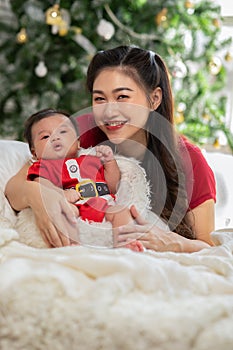 Beautiful Asian mom woman wear red cloth hugging newborn baby in christmas theme at cozy home.Happy infant baby looking at camera
