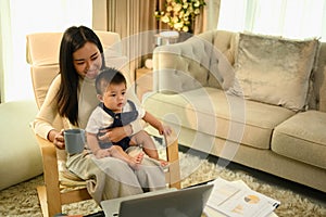 Beautiful Asian mother with baby son working on laptop at home