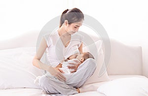 Beautiful Asian mother breast feeding her baby on bed at home, mom holding and looking toddler with love and tender. Milk from mom