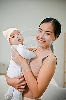 Beautiful Asian Mother holding her baby boy while relaxing in the living room