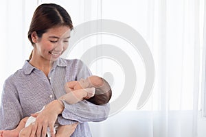 Beautiful Asian mother holding newborn baby while baby sleeping in her arms, Cheerful mom standing and lull adorable infant at