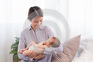 Beautiful Asian mother holding newborn baby while baby sleeping in her arms, happy mom looking adorable infant with love and