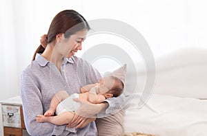 Beautiful Asian mother holding newborn baby while baby sleeping in her arms, happy mom looking adorable infant with love and