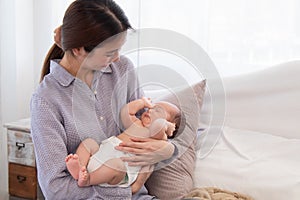 Beautiful Asian mother holding newborn baby while baby sleeping in her arms, happy mom looking adorable infant with love and