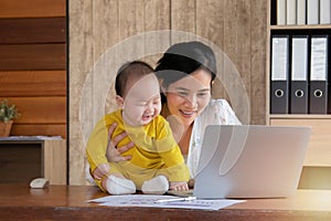Beautiful Asian mother spent time with curiosity toddler baby boy talking, playing on workplace home, adorable naughty son happy