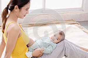 Beautiful Asian mother talking with toddler while baby lying on mother`s lap, young mom bonding with her adorable little baby at