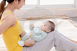 Beautiful Asian mother talking with toddler while baby lying on mother`s lap, young mom bonding with her adorable little baby at