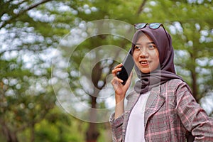 beautiful hijab muslim student calling her friend using smartphone in park