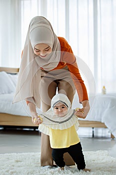 A beautiful Asian Muslim mother try to help the Muslim baby in a hijab dress for first walking on floor with love and care. Family