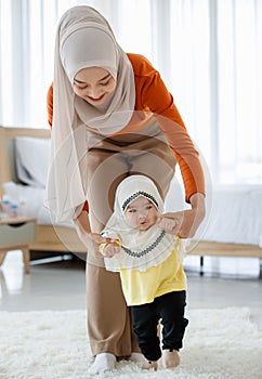 A beautiful Asian Muslim mother try to help the Muslim baby in a hijab dress for first walking on floor with love and care. Family