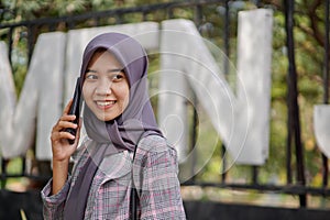 beautiful asian muslim student calling her friend using smartphone in park