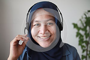 Beautiful Asian muslim woman using headphones speaking to camera, explaining something. Professional teacher mentor customer