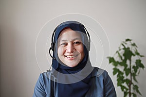 Beautiful Asian muslim woman using headphones speaking to camera, explaining something. Professional teacher mentor customer
