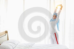 Beautiful asian muslim woman wearing white sleepwear, stretching her arms after getting up in the morning at sunrise. Cute young