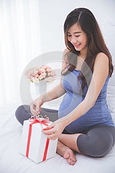 Beautiful asian pregnant woman accepting a gift, exciting to ope