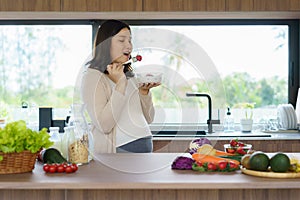 Beautiful Asian pregnant woman eating with lust cereals on breakfast in kitchen at home, enjoying meal. Yummy food for pregnant