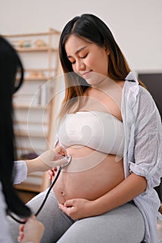 Beautiful Asian pregnant woman with her doctor in the clinic, listening a baby`s heartbeat