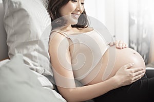 Beautiful asian pregnant woman lying on her bed, touching  big belly