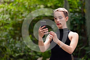 Queer LGBT community supporter man with mustache wearing jumpsuit using phone outdoors in park photo