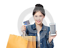 Beautiful Asian stylish young woman in jeans shirt is holding shopping bags, smartphone, credit card and smiling isolated on white