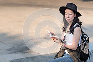 Beautiful asian tourist woman looking at travel guide book for searching location of landmark