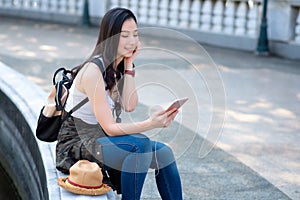Beautiful asian tourist woman relaxing and enjoying listening the music on a smartphone in urban city downtown