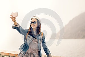 Beautiful Asian traveler taking selfie with ocean view background, soft warm light tone