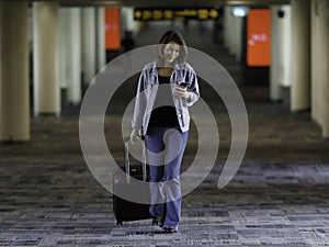 Beautiful Asian traveler wearing casual dress holding bag using smartphone and walking in airport terminal walkway