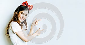 Beautiful asian university or college student woman wearing funny bow headband, pointing at copy space on whiteboard background