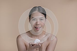 Beautiful Asian woman applying moisturiser cream. Photo of smiling woman with perfect makeup on beige background.