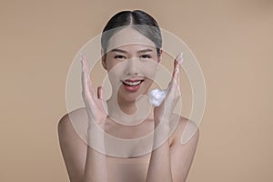Beautiful Asian woman applying moisturiser cream. Photo of smiling woman with perfect makeup on beige background.