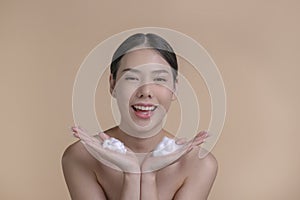 Beautiful Asian woman applying moisturiser cream. Photo of smiling woman with perfect makeup on beige background.