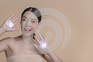 Beautiful Asian woman applying moisturiser cream. Photo of smiling woman with perfect makeup on beige background.