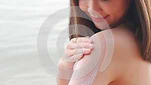 Beautiful Asian woman applying sun protection cream on tanned shoulder on the beach