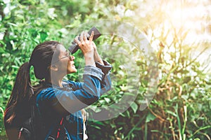 Beautiful Asian woman with binoculars telescope in forest looking destination. People lifestyles and leisure activity. Nature and