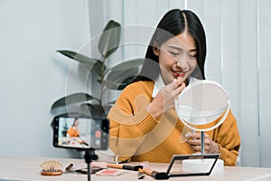Beautiful asian woman blogger using camera phone recording vlog video live streaming and showing how to make up cosmetics at home