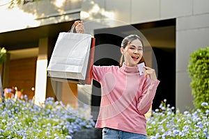 Beautiful Asian woman carrying shopping bags and credit card, standing outside of the mall