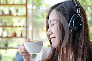 A beautiful Asian woman close her eyes and listening to music with headphone while drinking coffee with feeling happy and relax in