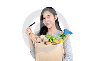 Asian woman with credit card holding paper bag full of groceries isolated on studio white background