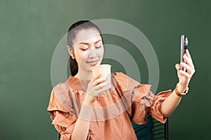 Beautiful Asian woman customer drinking hot coffee while taking selfie shot with takeaway coffee cup in coffee shop