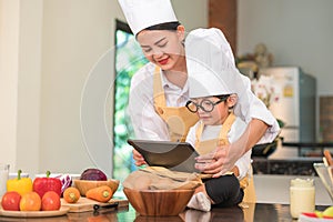 Beautiful Asian woman and cute little boy with eyeglasses prepare to cooking in kitchen at home with tablet. People lifestyles and
