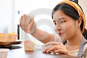 Beautiful Asian woman decorating home made cupcake in the kitchen