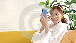 Beautiful Asian woman doing spa at home holding a smartphone