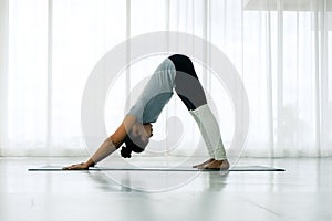 Beautiful Asian woman doing yoga exercise in the white room, downward facing dog pose, adho mukha svanasana